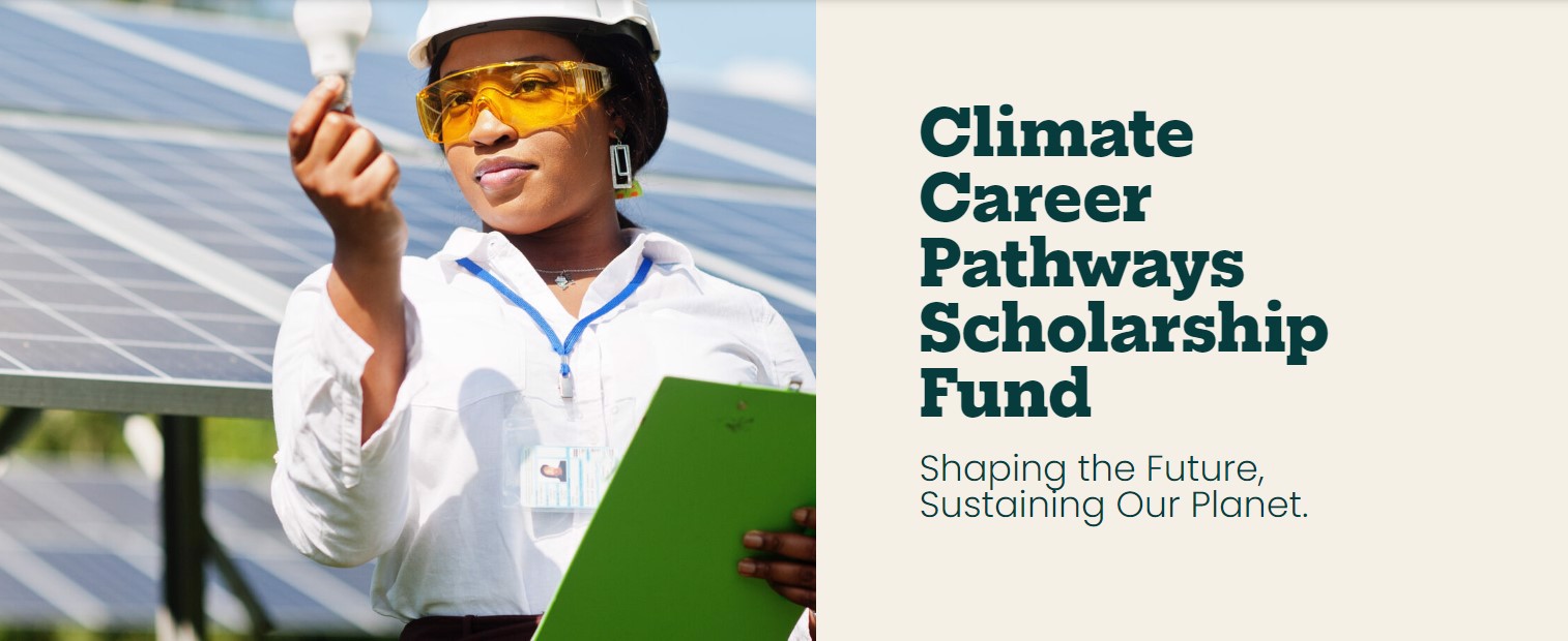 A woman of color in a hard hat, protective glasses, white shirt, and nametag around her neck holds up a lightbulb in one hand and a green clipboard in the other while standing in front of solar panels. 