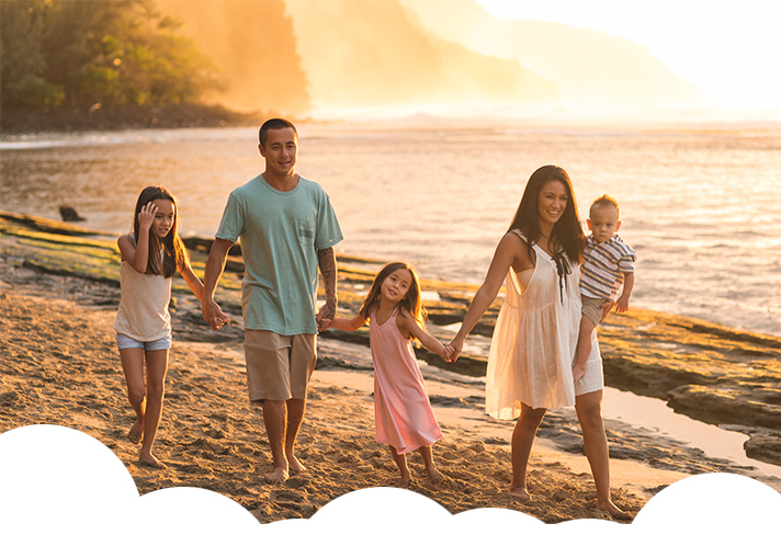 Family enjoying breath-taking walk along hawaii beach with mountain view behind them.