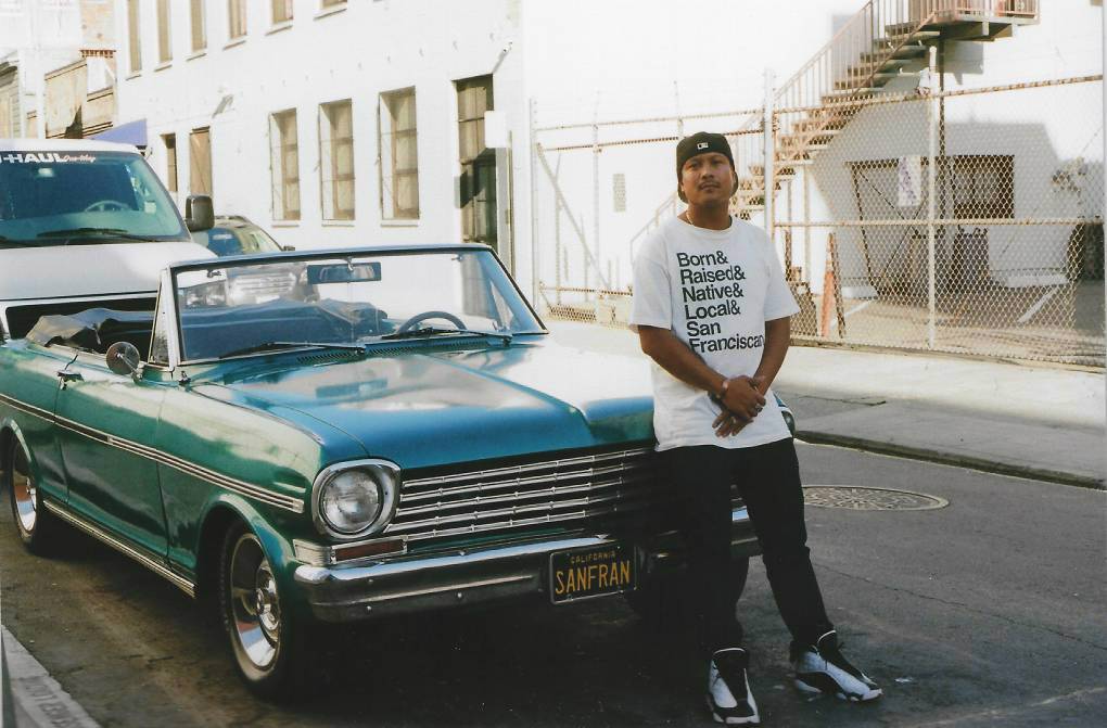 Harvey Lozada stands in front of a green car.