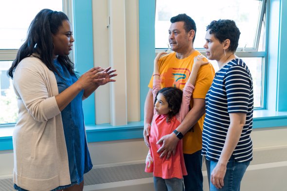 A black female adult stands with a mother, father, and young child in a hallway.