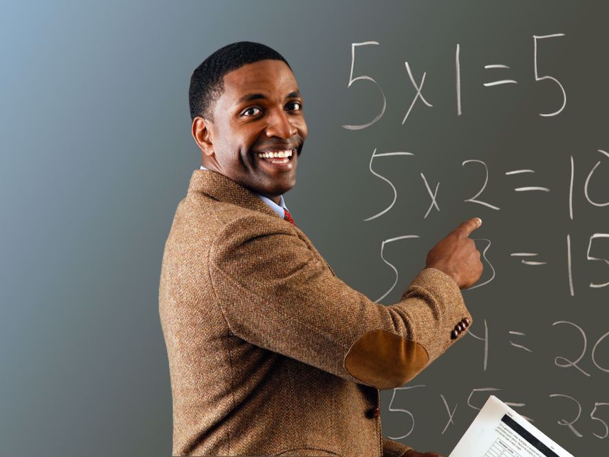 Teacher writing multiplication table on blackboard