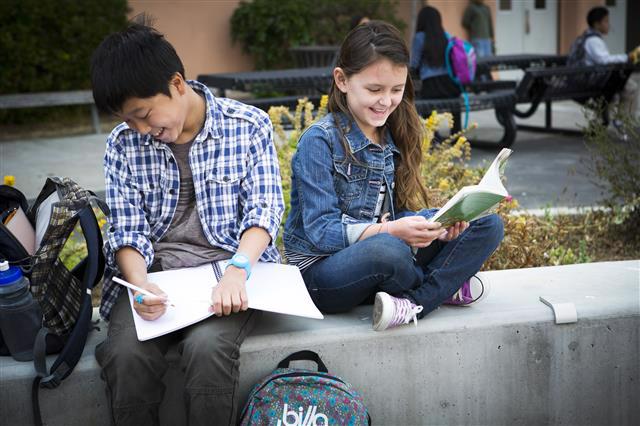 Two kids sitting outside reading books.