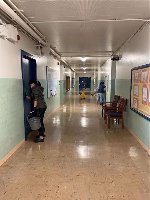 Facilities staff clean doors in a school hallway.