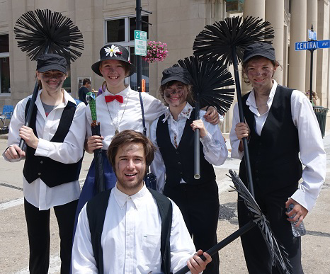 A group of five white people stand in an intersection dressed as chimney sweepers