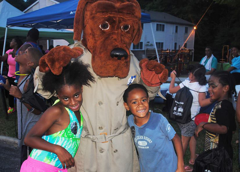 A mascot stands with two black children at National Night Out