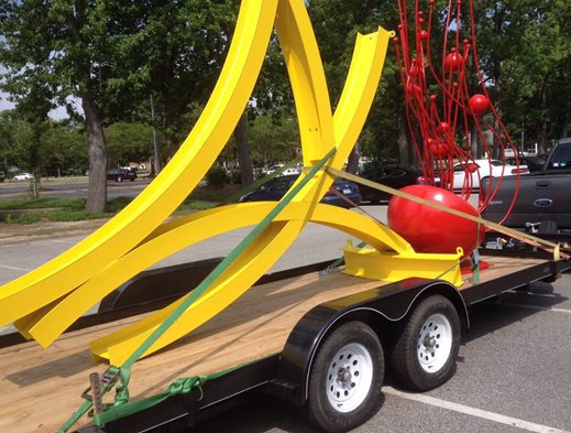 A yellow and red public art sculpture is being transported