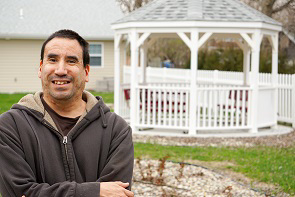 A man wearing a gray hoodie stands in front of a white gazebo