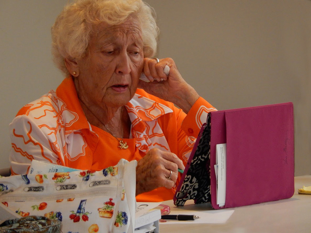 A senior white woman wearing an orange and white shirt looks at her tablet