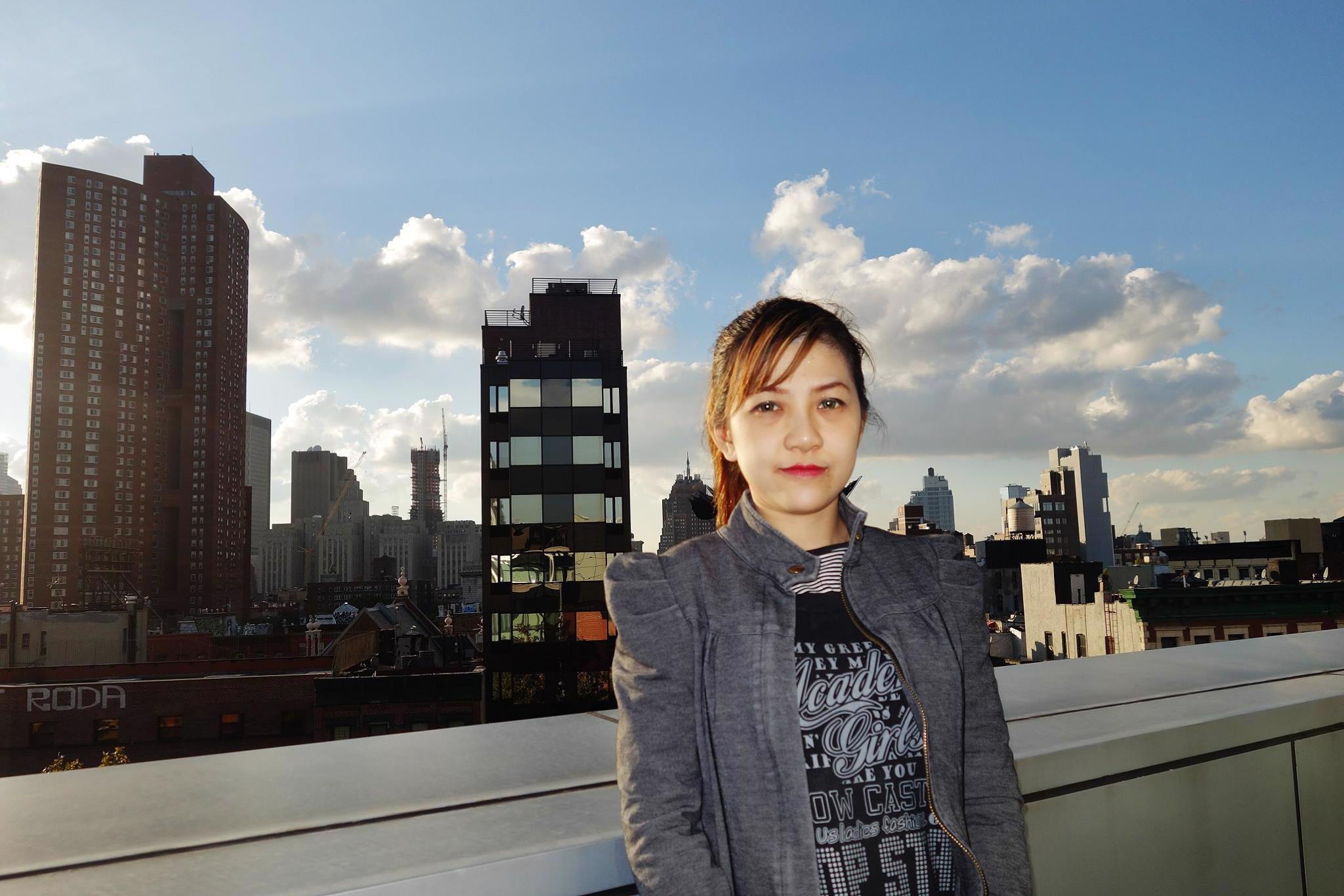 A young woman standing on the rooftop of a building with a view of New York City in the background.