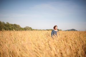 A white woman stands in the middle of a wheat field