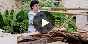 A video still of a boy picking up broken pieces of wood