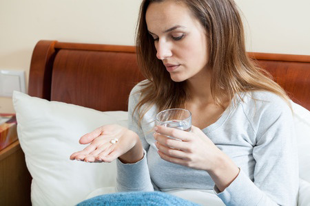Woman sitting in bed looking at pills in her hand