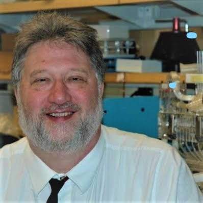 Photo of Paul Ernsberger, a smiling fat white male with a full beard wearing a white shirt and tie in a laboratory setting