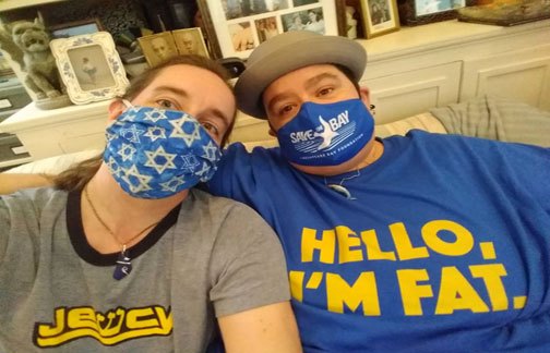 An array of A couple selfie of Mycroft Masada and Julia McCrossin. Mycroft is thin and femme-presenting, Julia is superfat and mas(s)culine-presenting; they are both white with brown hair, and wearing masks, earrings and pendants; Julia is wearing a men's hat. Mycroft's mask has Magens David, Julia's has the Chesapeake Bay Foundation logo. Mycroft's t-shirt says "Jewcy" and the W is the Hebrew letter shin, Julia's says "HELLO, I'M FAT."three pictures of fat Asian American and Pacific Islanders in outdoor settings: on the left, a young Asian femme carrying an umbrella; in the middle, a young Asian masc at a soccer match; on the right, a young Pacific Island femme outside a cabin.