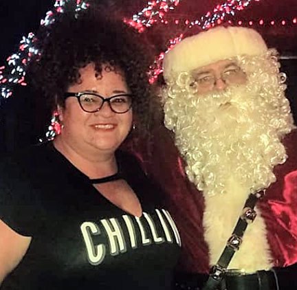 A waist-up photo of Tigress Osborn, a fat woman of color, next to Santa Claus