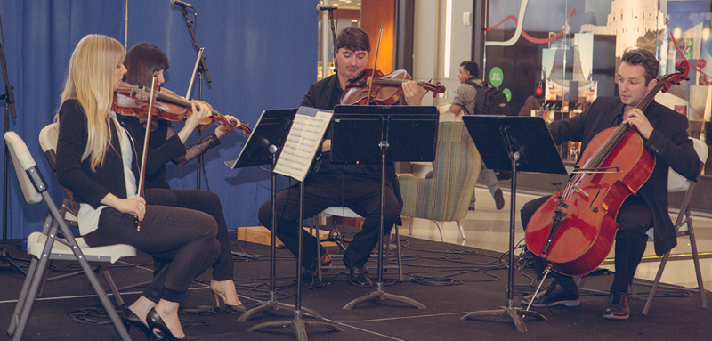 Image of a string quartet, the quartet consist of two women and two men, on a small stage in one of the terminals.