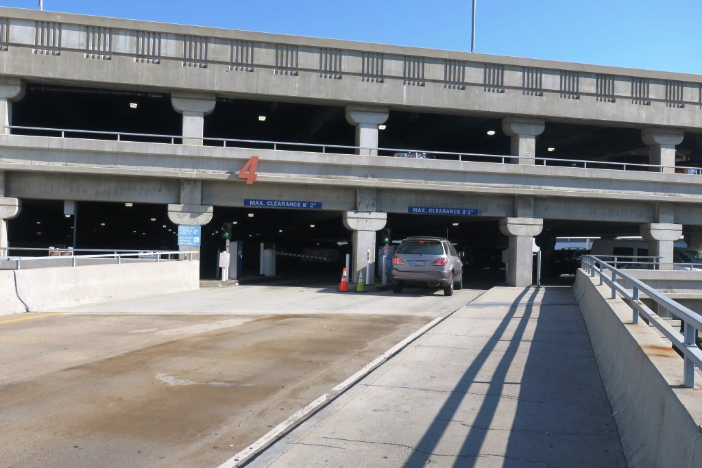 Image of road leading to an upper level entrance to parking structure 4. Only one vehicle is pulling a ticket to enter. The sructure is made of concrete. 