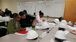 Image of the HireLAX students in a classroom setting, it is the first day of classes and on each desk there is a brand new white hard hat.